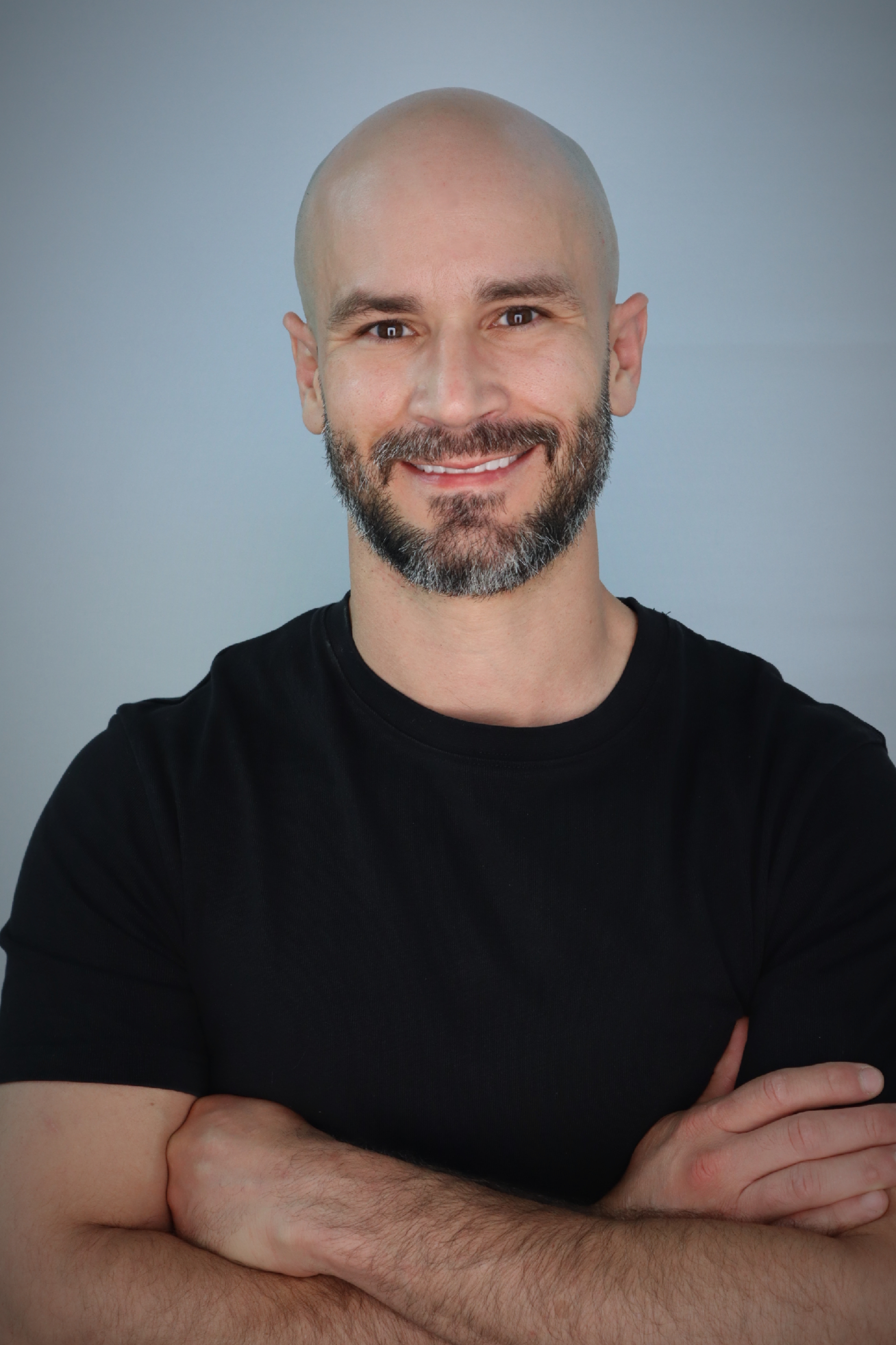 Smilling man with light-tan complexion and dark beard corssing his arms